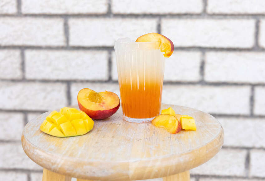 Styled peach mango drink with fresh fruit on a wooden stool