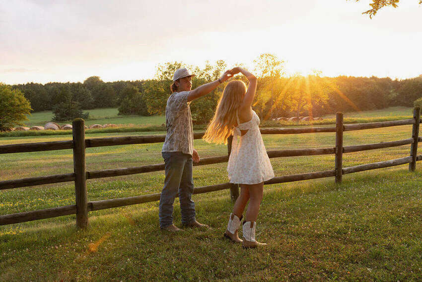Couple dancing together at golden hour by a wooden fence
