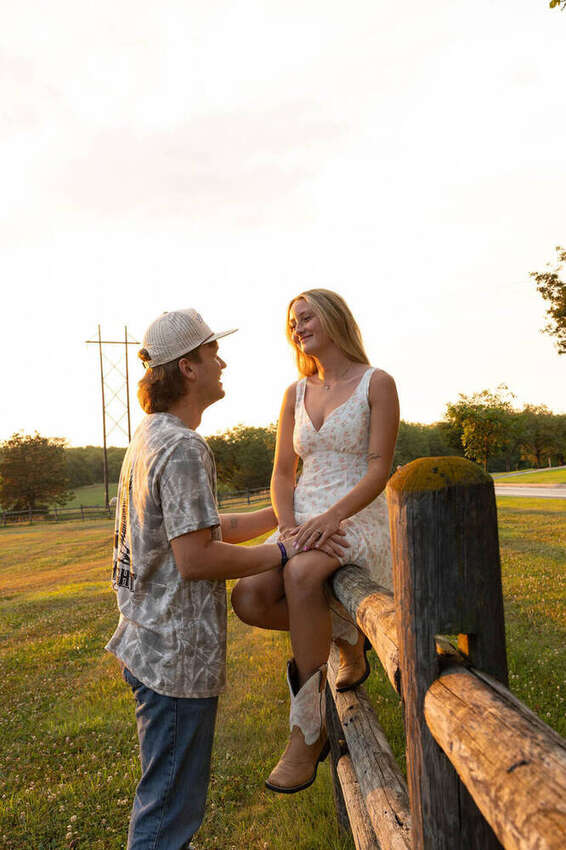 Couple talking, she's sitting on a wooden fence at sunset