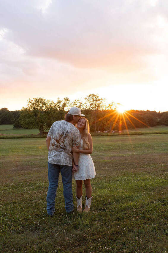 Couple embracing, he's kissing her forehead at sunset in a field