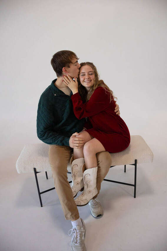 Couple embracing in a studio session, she's wearing a red dress and cowboy boots