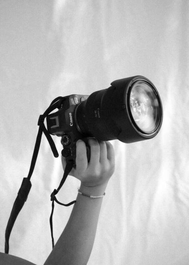 Black and white close-up of a hand holding a camera raised in the air