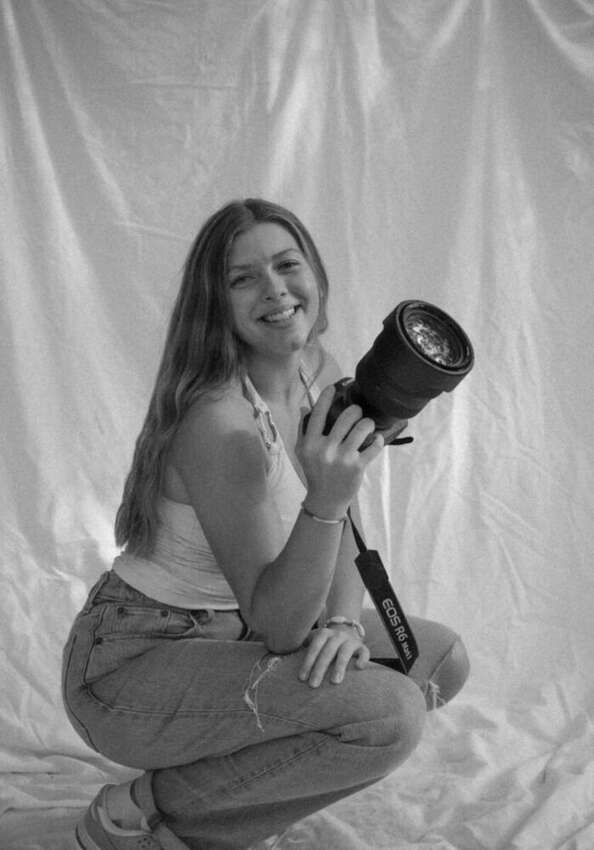 Black and white photo of Isabella crouching and smiling while holding her camera