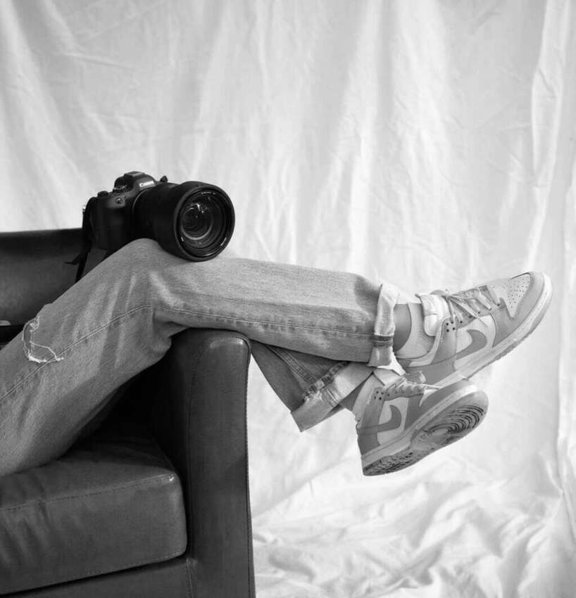 Black and white photo of a camera resting beside sneakers on a couch
