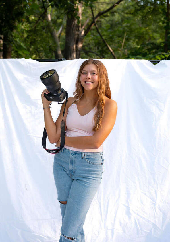 Isabella standing outdoors holding her camera and smiling