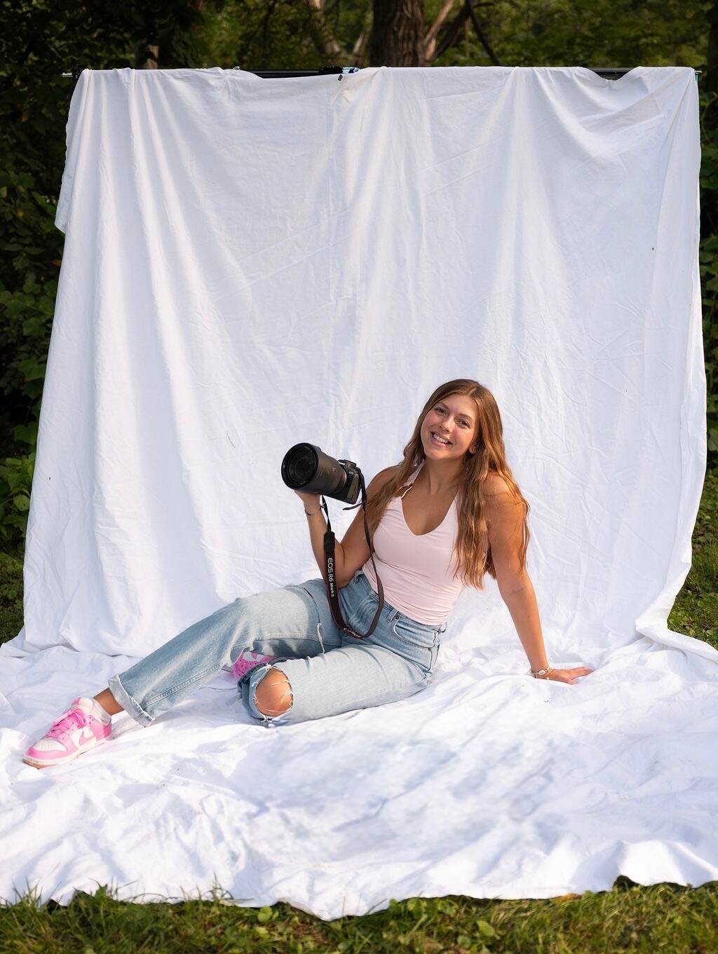 Isabella sitting and smiling while holding her camera in front of a white backdrop