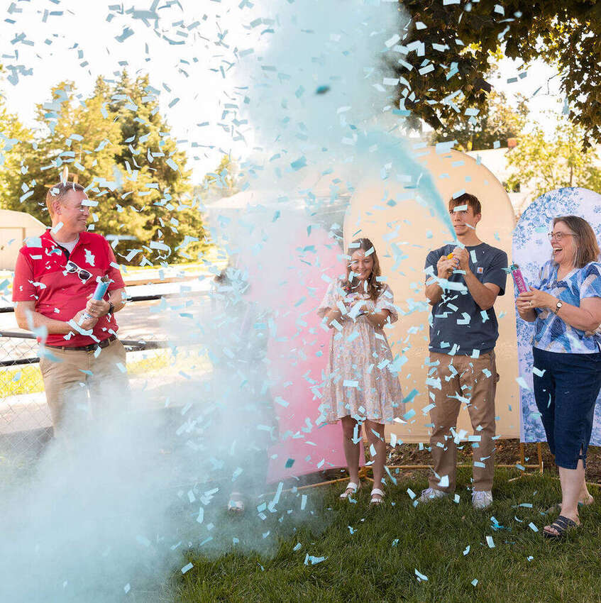Family celebrating a gender reveal with blue confetti poppers, second angle