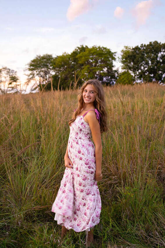 Senior portrait of a girl in a pink floral dress in a field