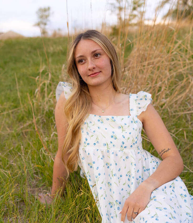 Senior portrait of a girl in a blue floral dress lying in the grass