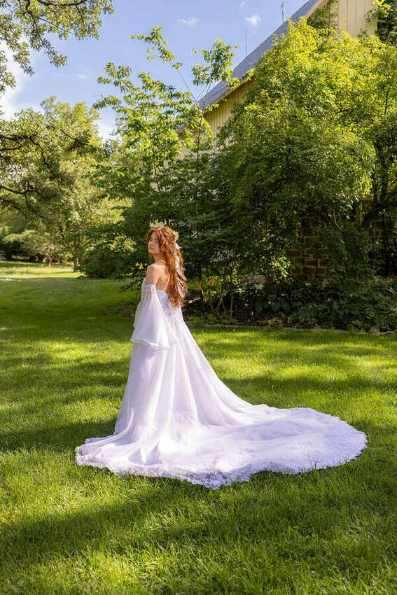 Bride in a flowing white dress standing on a lawn, back view