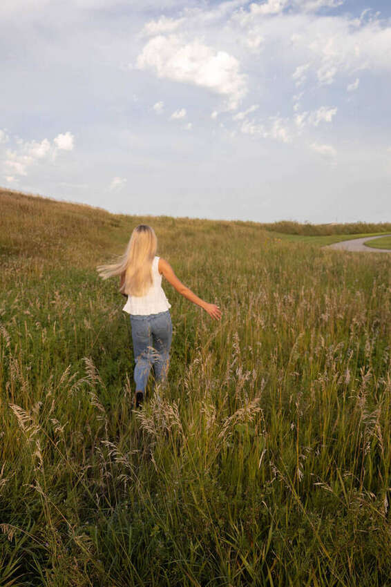 Senior girl walking away through a grassy hillside, back view