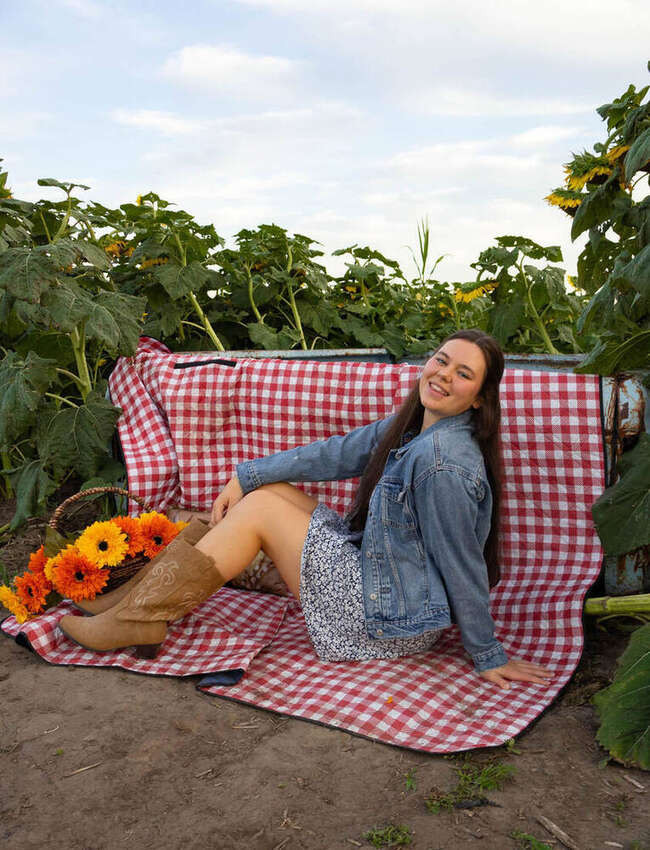 Senior portrait of a girl sitting in a sunflower field with a picnic blanket