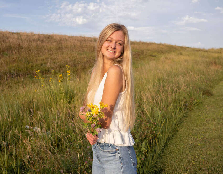 Senior portrait of a girl holding wildflowers in a golden field