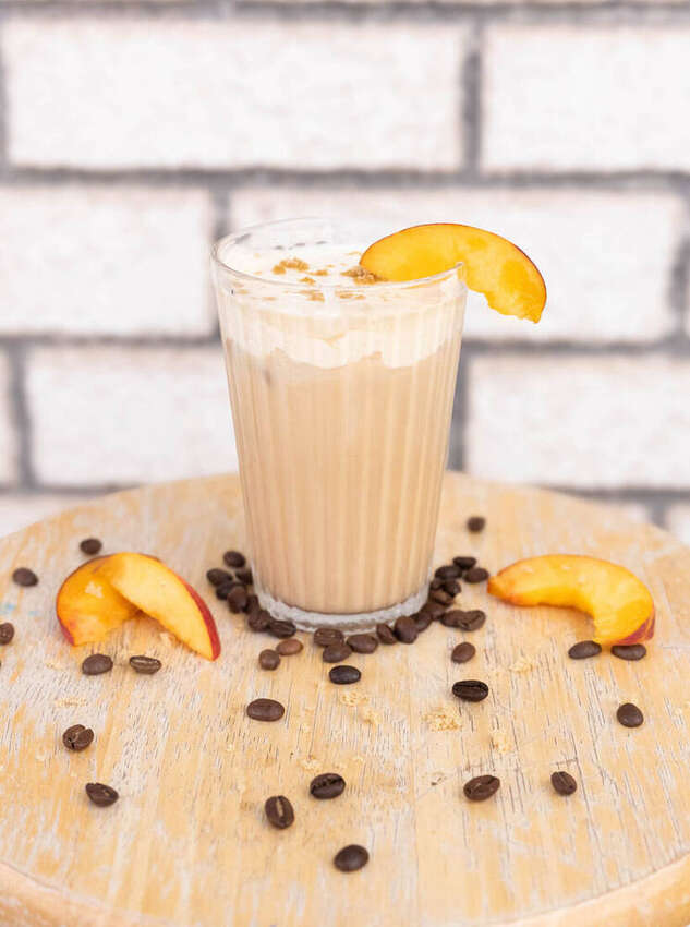 Styled iced latte with coffee beans and a peach slice